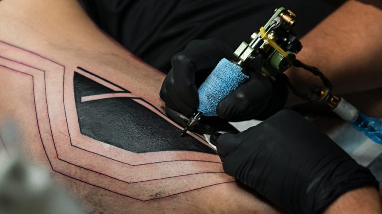 Professional tattoo artist uses a tattoo machine to make a tattoo on a man's leg.